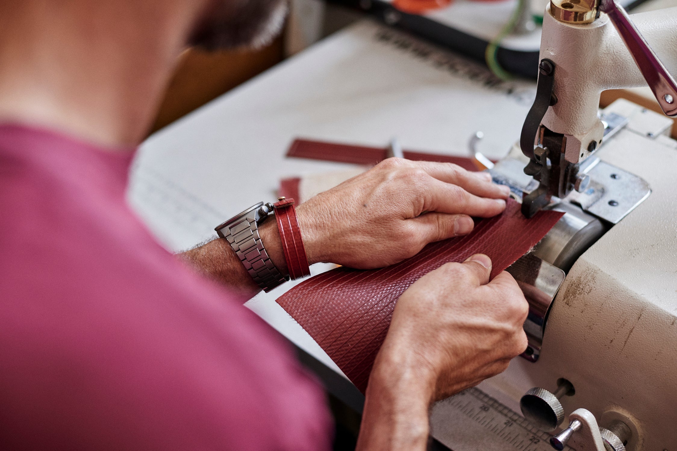 Photo of a man's hands as he works at a sewing table with a piece of red fire hose.
