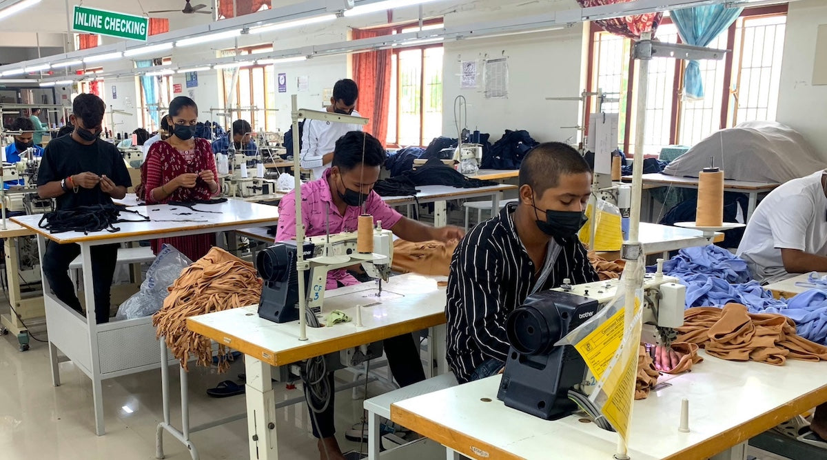 workers inside a garment factory seated at workstations and sewing YOU bralettes