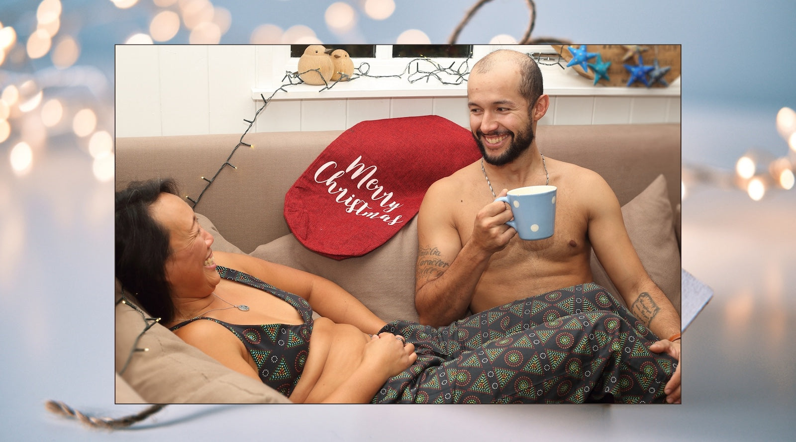 model wearing YOU black mara pyjamas and bralette lying on a sofa with another model with christmas decorations around.