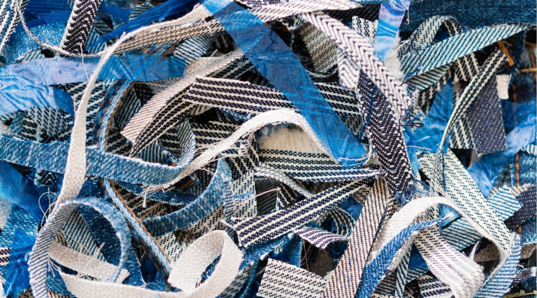 Close up photo of a bundle of thin shredded strips of blue, black, and white textiles.