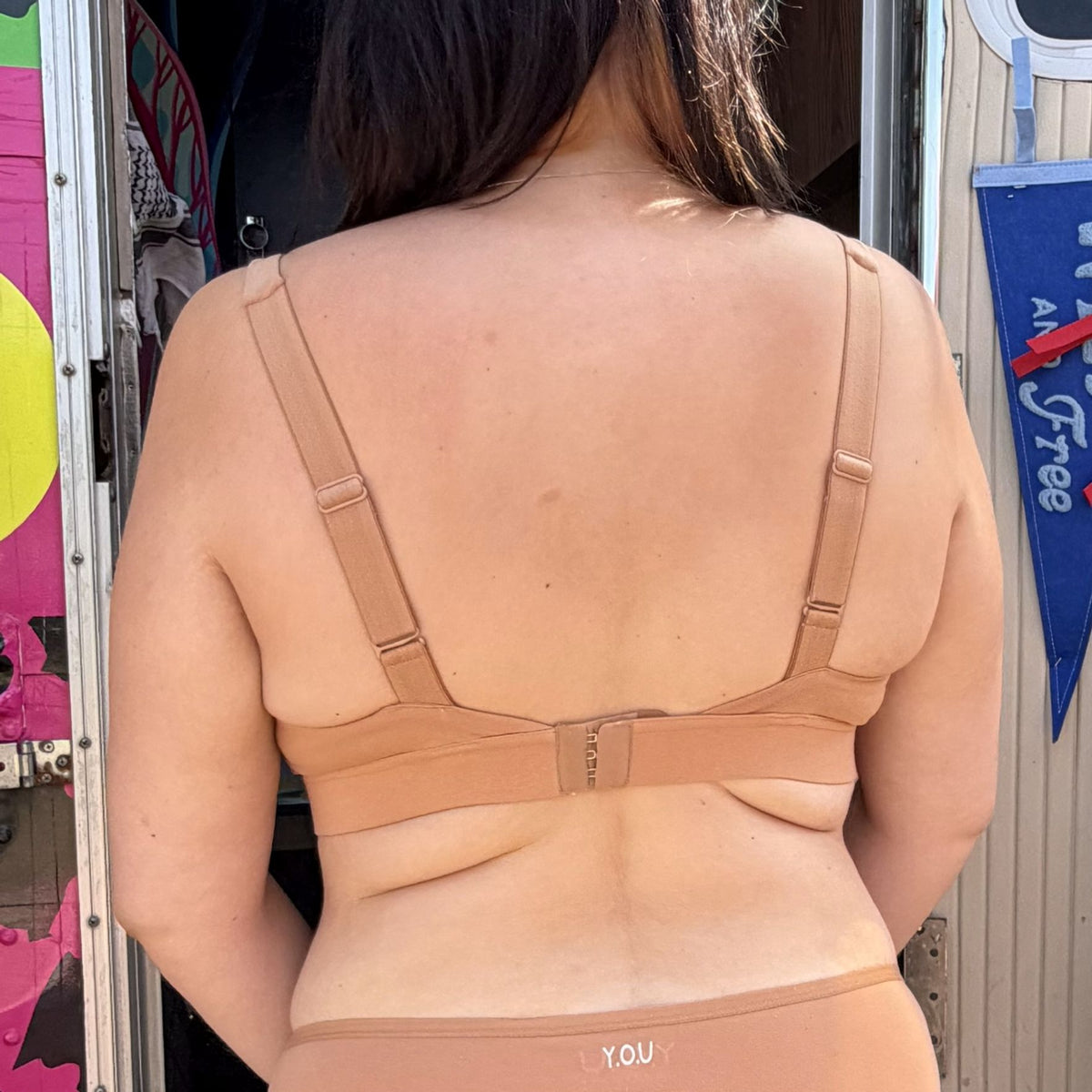 A photo of a model wearing the YOU Underwear non wired bra in almond. She is standing facing away from the camera and the photo is zoomed so we can see from her shoulders to just below her hips.