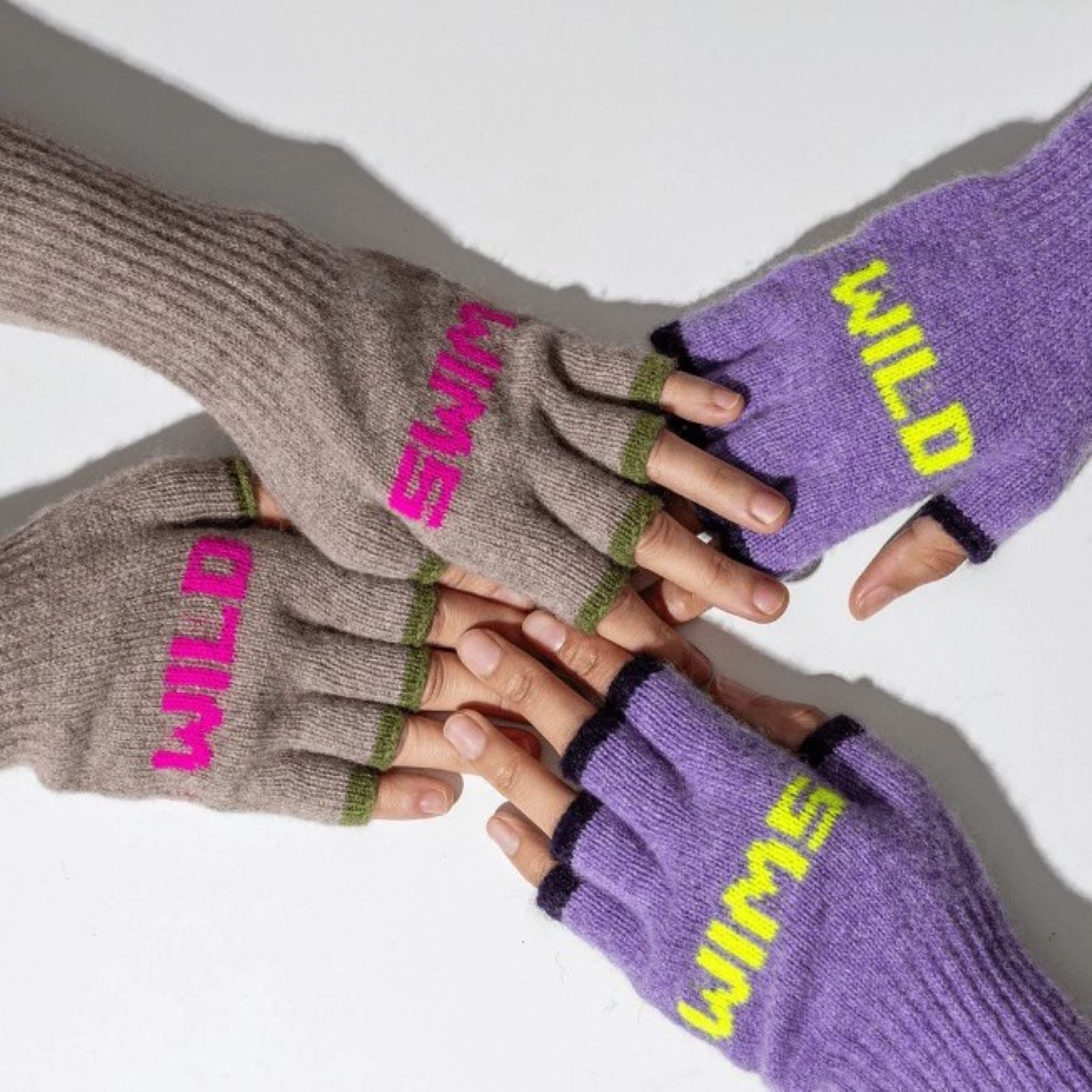 A photo of two pairs of hands both wearing the Black & Beech Wild Swim gloves, with a white background behind them. One person is wearing the purple pair with neon yellow writing and the other is wearing the beige oatmeal with neon pink.