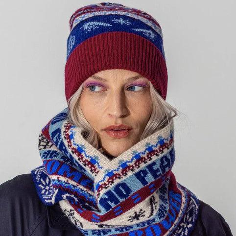 A model wearing the Black & Beech fairisle beanie and scarf in klein and burgundy. She is wearing pink eye shadow and standing in front of a white background