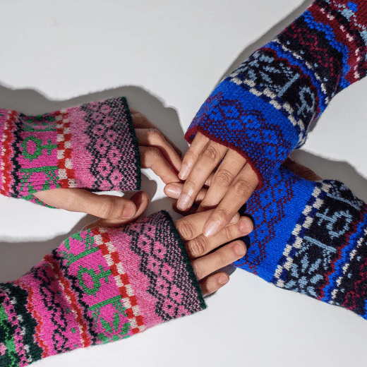A photo of two people wearing the Black and Beech Fairisle Wrist Warmers, one wearing the pink and one wearing blue. They are holding hands on a white background.