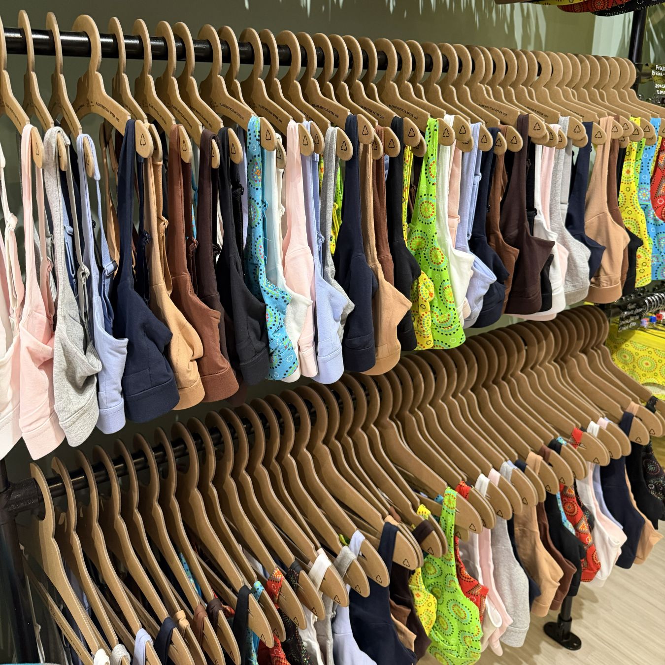 A photo of the YOU Underwear bra rails in the Brighton shop. The image is close up to the bras, showcasing their bright colours. They are neatly hung on wooden hangers and we can see two rails which are vertical to each other.