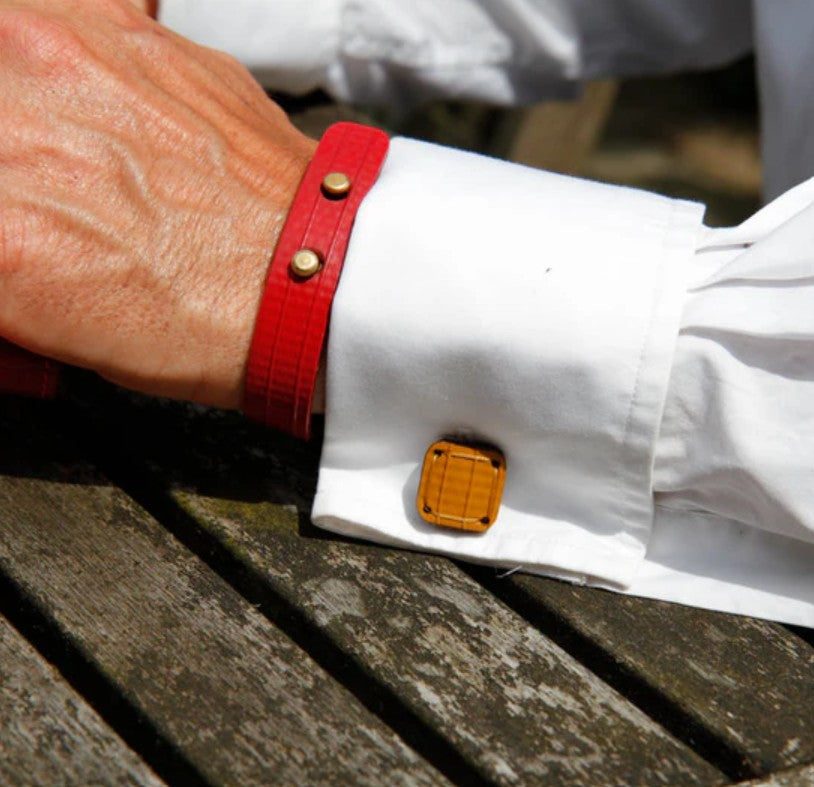 A zoomed in photo of man wearing the yellow Elvis and Kresse cufflinks with a white shirt and red bracelete on the background of wooden picnic bench