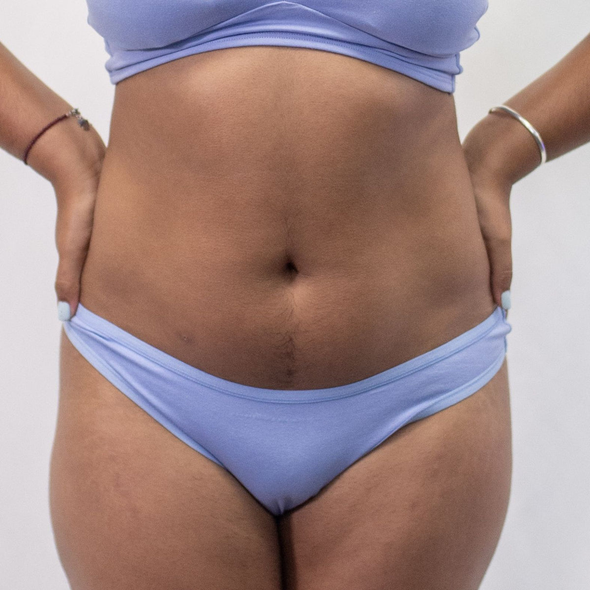 A photo of a model wearing the YOU Underwear thong in light blue. The model is standing facing the camera with their hands on their hips. The photo is zoomed in so we can see from the model's stomach to their upper thigh. The background is white.