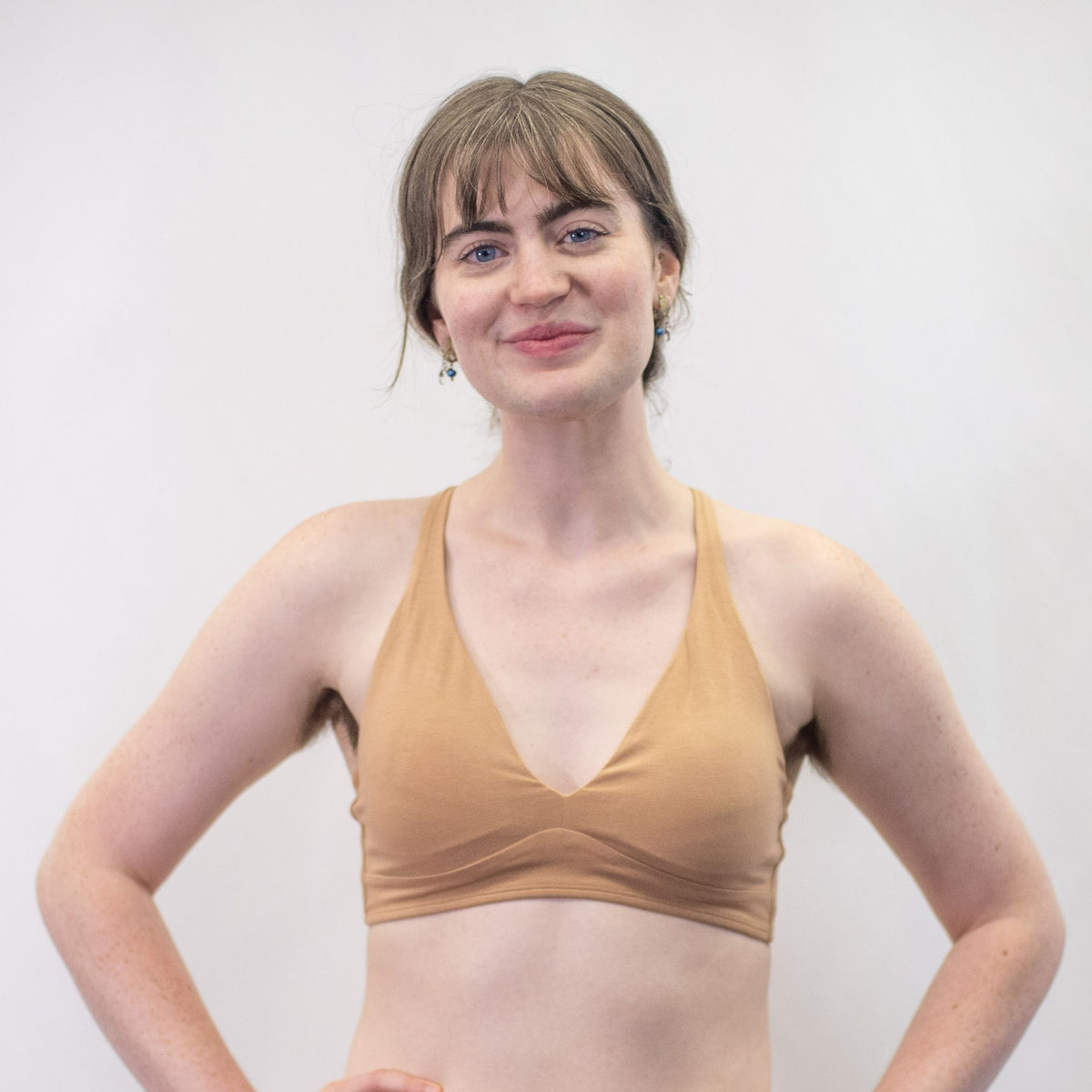 A photo of a model wearing the YOU Underwear padded bralette in almond. The model is standing facing the camera with both hands on their hips. The photo is cropped so we can see to the model's waist. There is a white background.