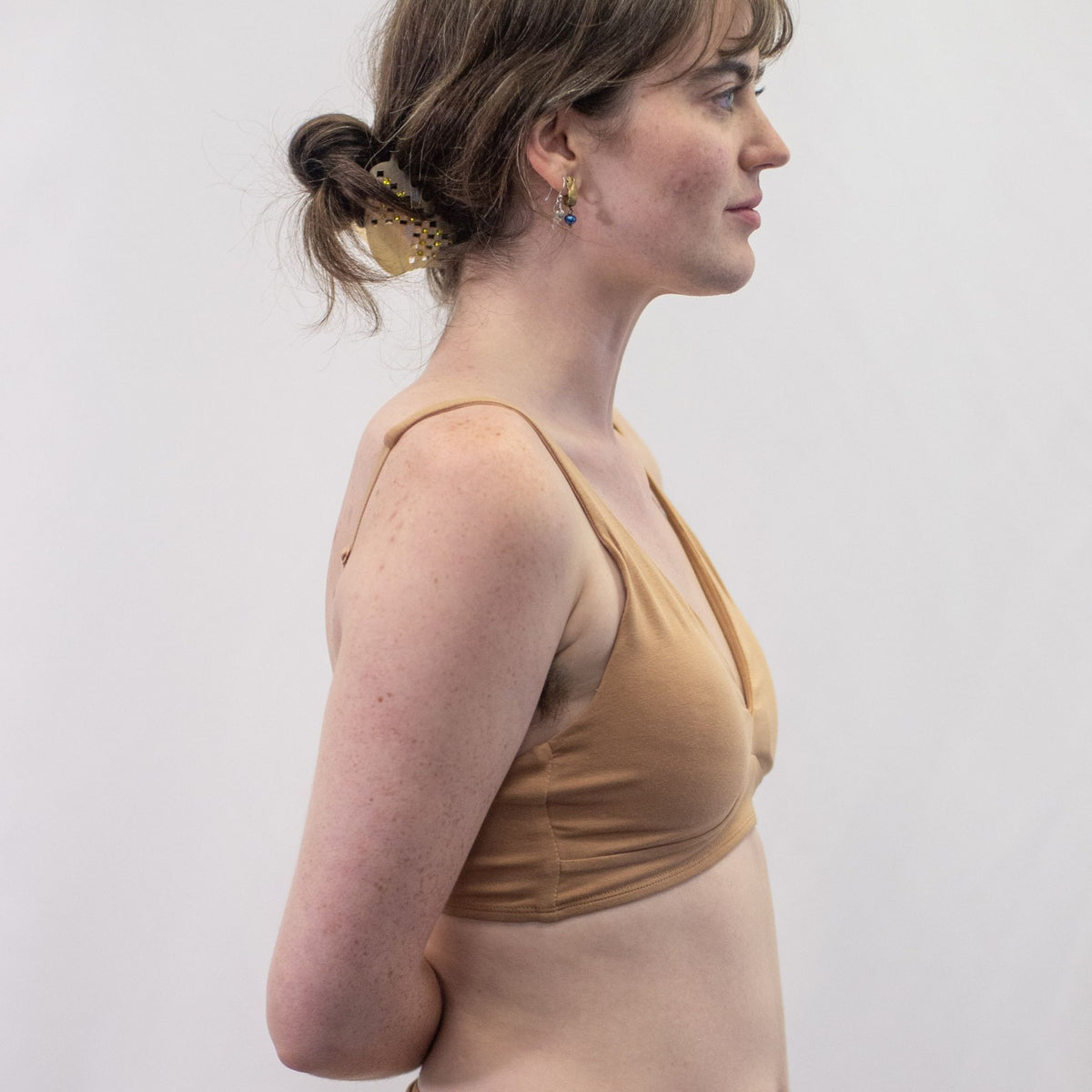 A photo of a model wearing the YOU Underwear padded bralette in almond. The model is standing side on to the camera with her hands behind her back. The photo is cropped so we can see to the model's waist. There is a white background.