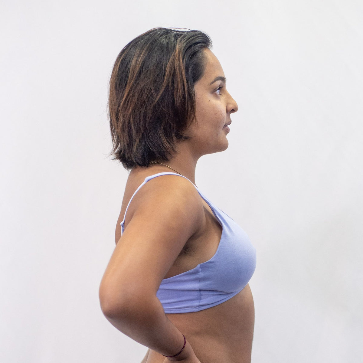 A photo of a model wearing the YOU Underwear padded bralette in light blue. She is standing side on to the camera with both hands on her hips. The photo is cropped so we can see to the model's waist. There is a white background.
