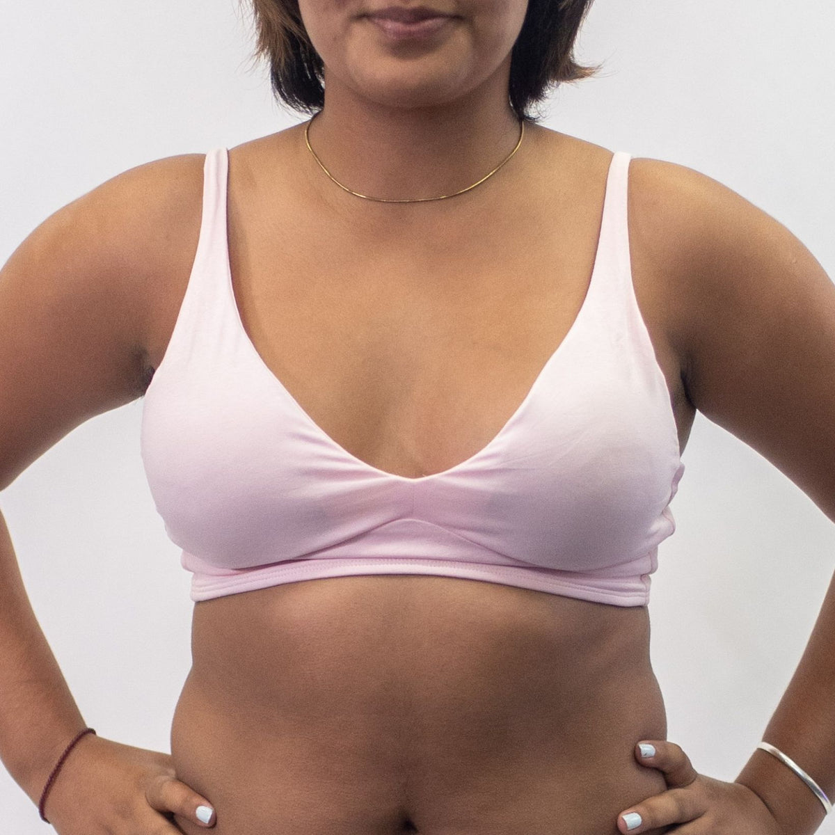 A photo of a model wearing the YOU Underwear padded bralette in pink. She is standing facing the camera with both hands on her hips. The photo is cropped so we can see from the model's jaw to their waist. There is a white background.
