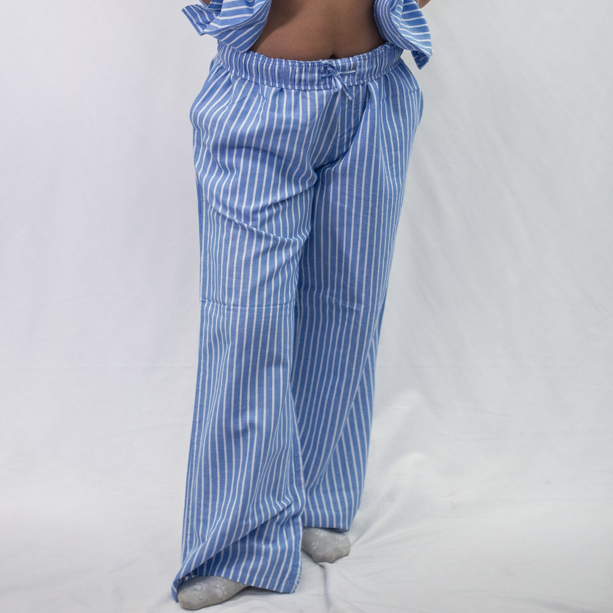 A photo of a model wearing the YOU Underwear woven pyjama bottoms in the classic blue and white stripe. The photo is zoomed in so we can see from the model's stomach to the floor. They are standing face onto the camera and there is a white background behind them.