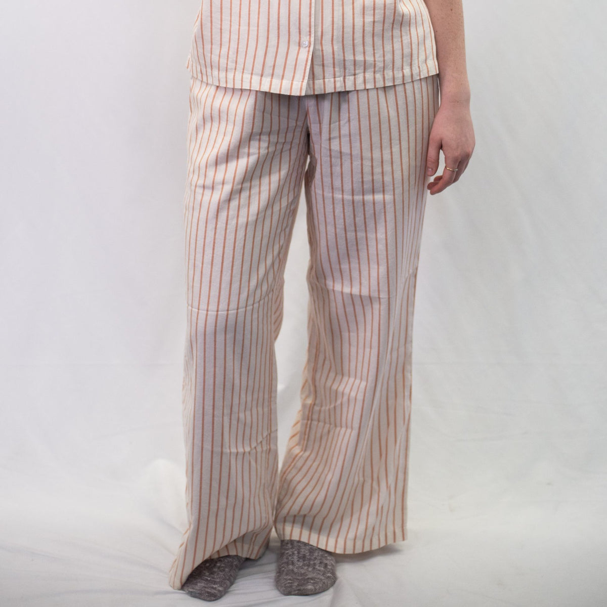 A photo of a model wearing the YOU Underwear woven pyjama bottoms in soft cream and coral. The photo is zoomed in so we can see from the model's stomach to the floor. They are facing the camera and there is a white background.