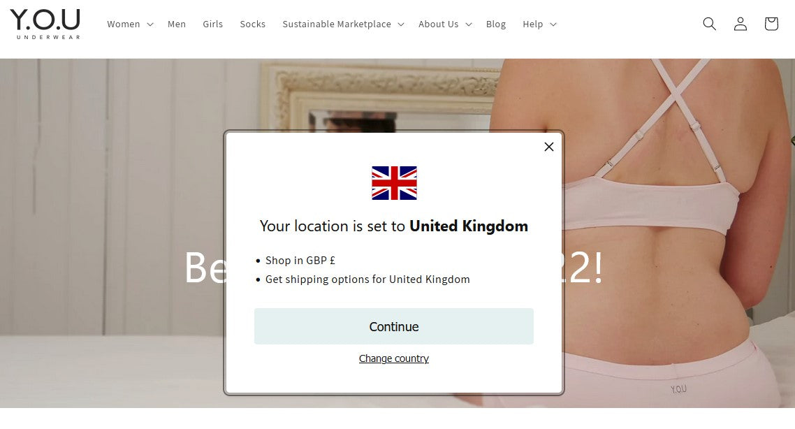 Screenshot of the Y.O.U underwear homepage showing the UK country selector on top of a lady sitting on a bed wearing a pink underwear set