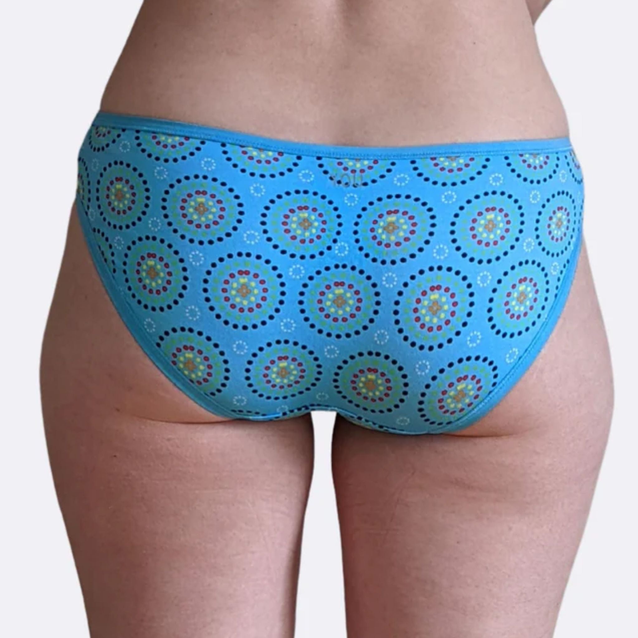 Person wearing blue bikini bottoms with circular patterns, showing the back view