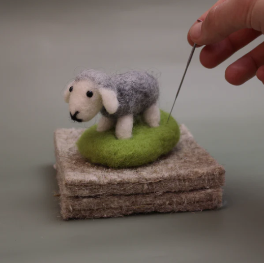 Felted sheep toy on a stack of felted blocks with a hand holding a needle.