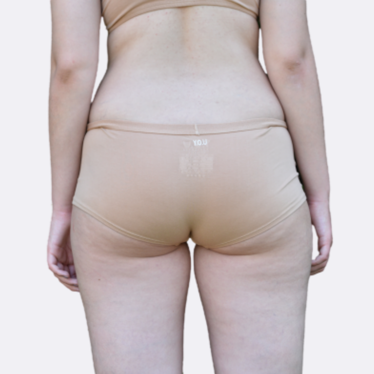 Model with light skin and purple nail polish wears organic cotton plain almond light nude boy shorts and faces the back