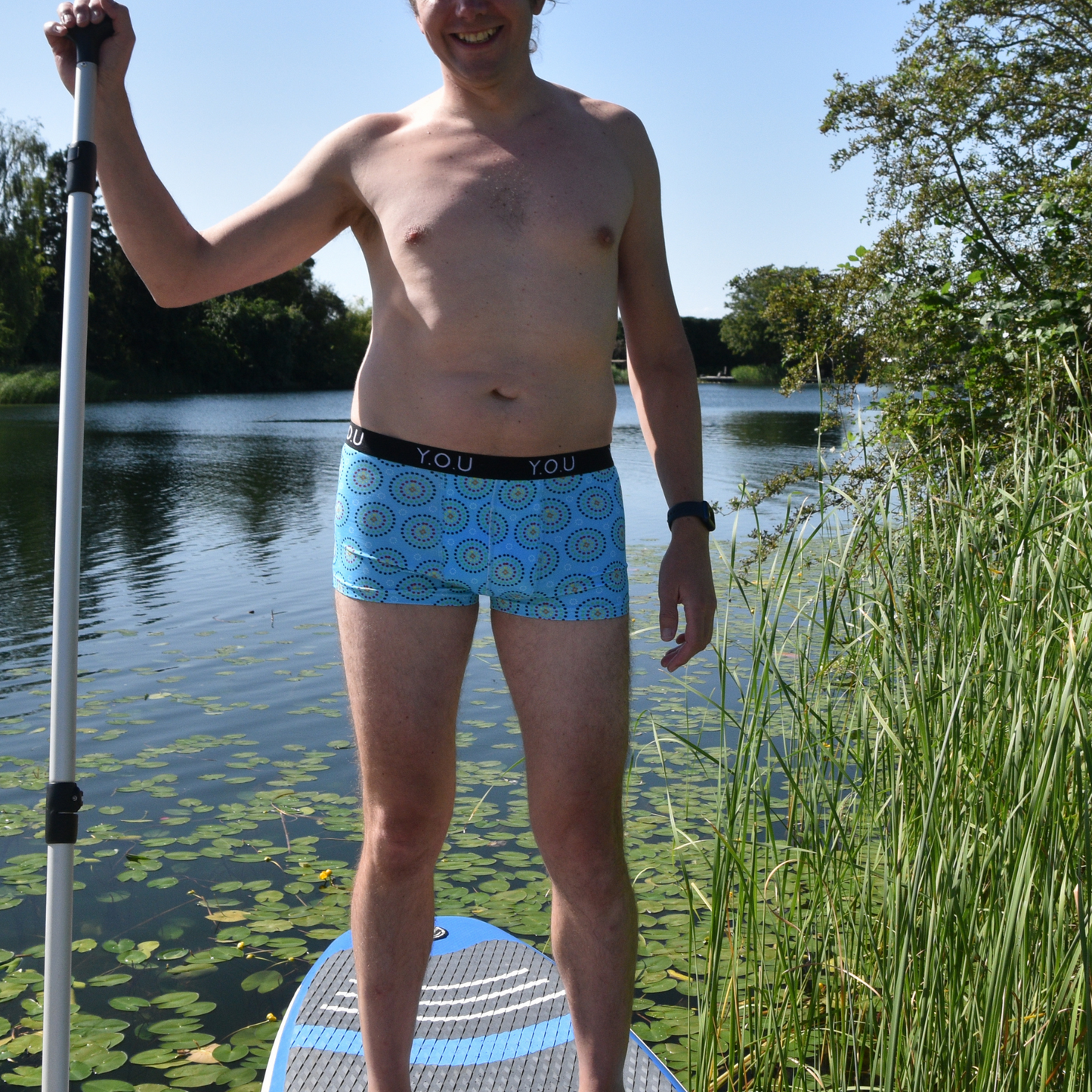 a man is wearing Blue Mara Short Trunks whilst stood on a paddleboard