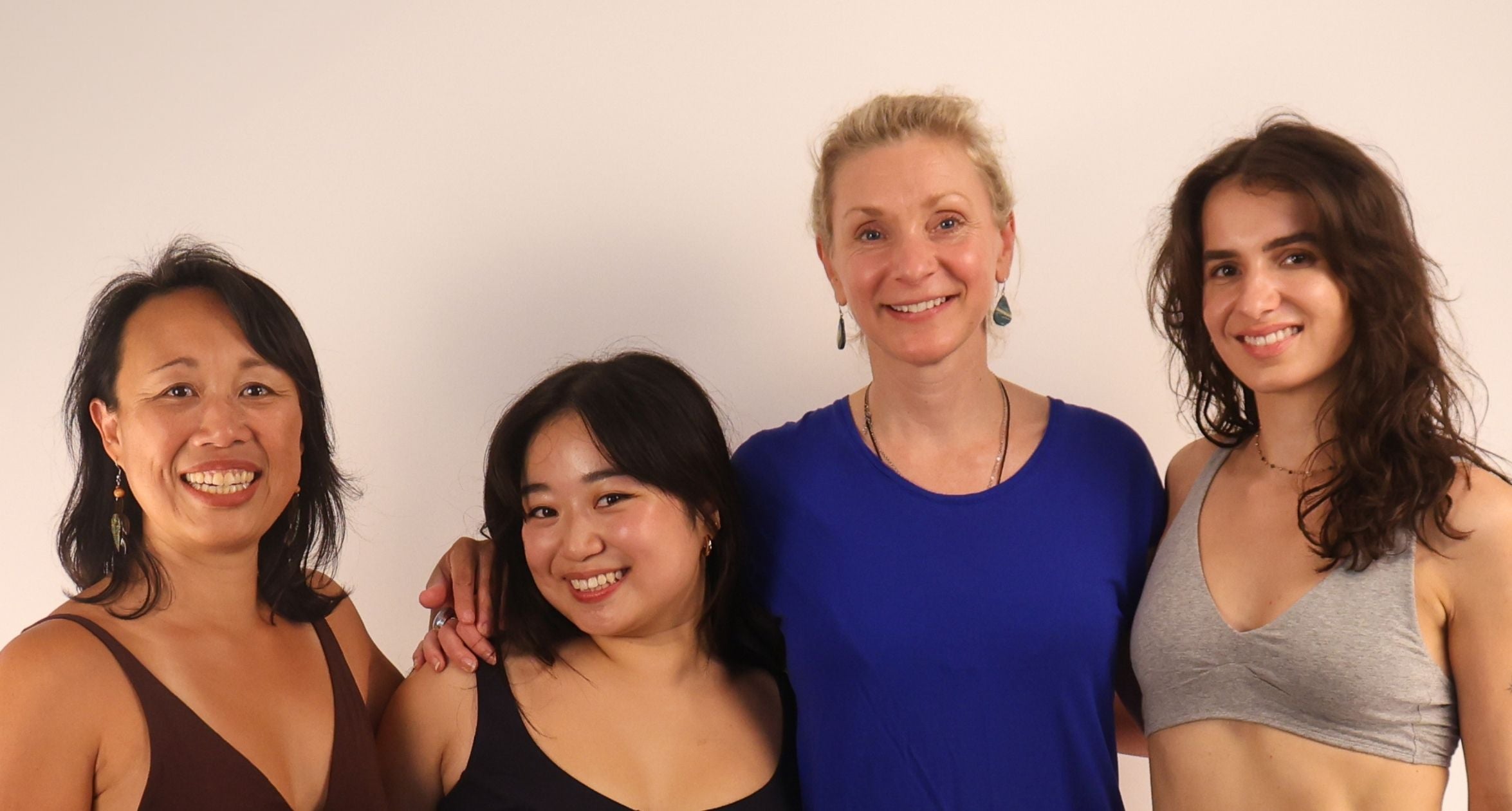 four women standing with their arms around each other and smiling towards the camera. Three of the women are wearing Y.O.U organic cotton bras and one woman wears a blue t shirt.