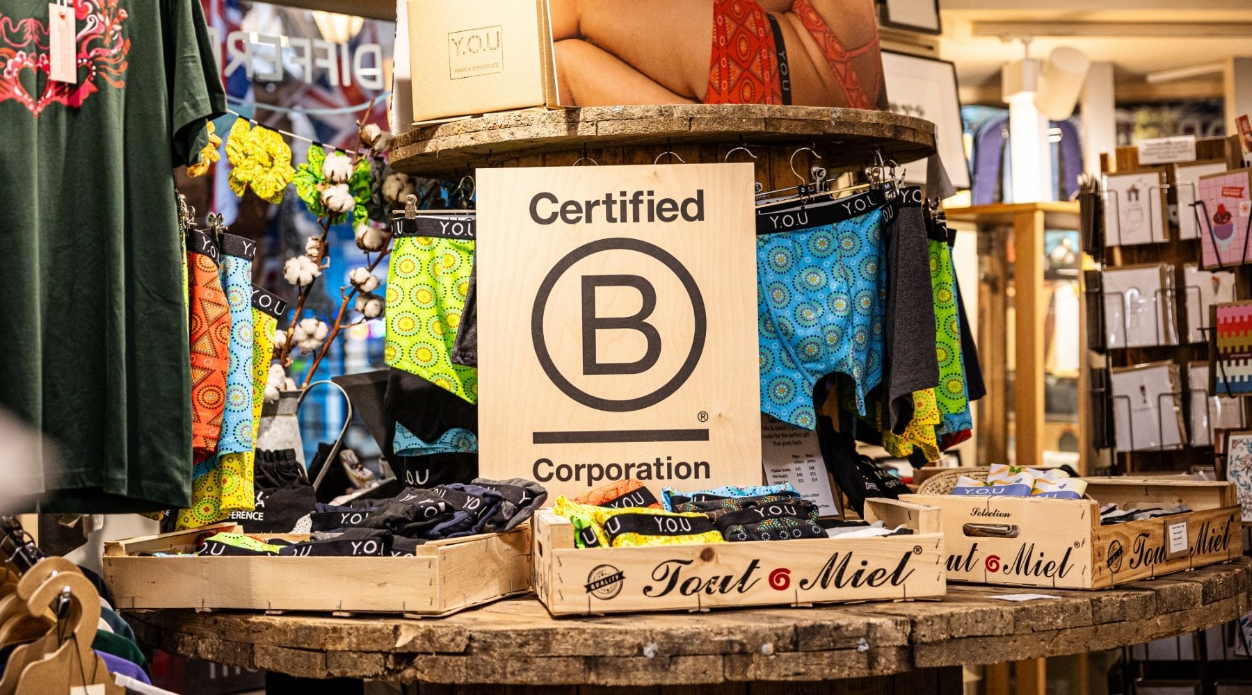 a large wooden sign with a black B Corp logo printed on the top, standing behind a display of organic cotton men's Y.O.U underwear