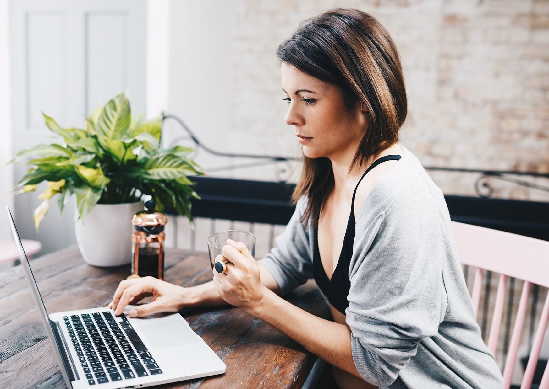 A dark haired woman sits at a wooden desk and uses her laptop. She's wearing a light blue shirt and Y.O.U Underwear black organic cotton underwear