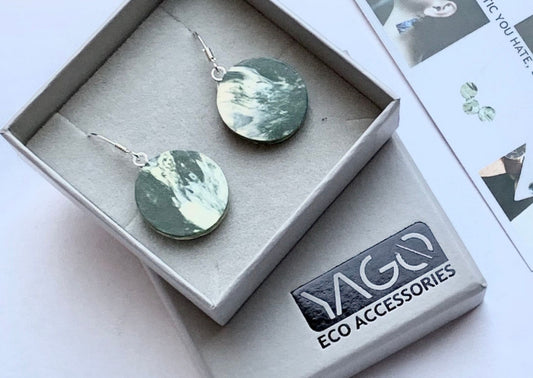 A paid of circular green and cream earrings in light grey boxes. In between the boxes