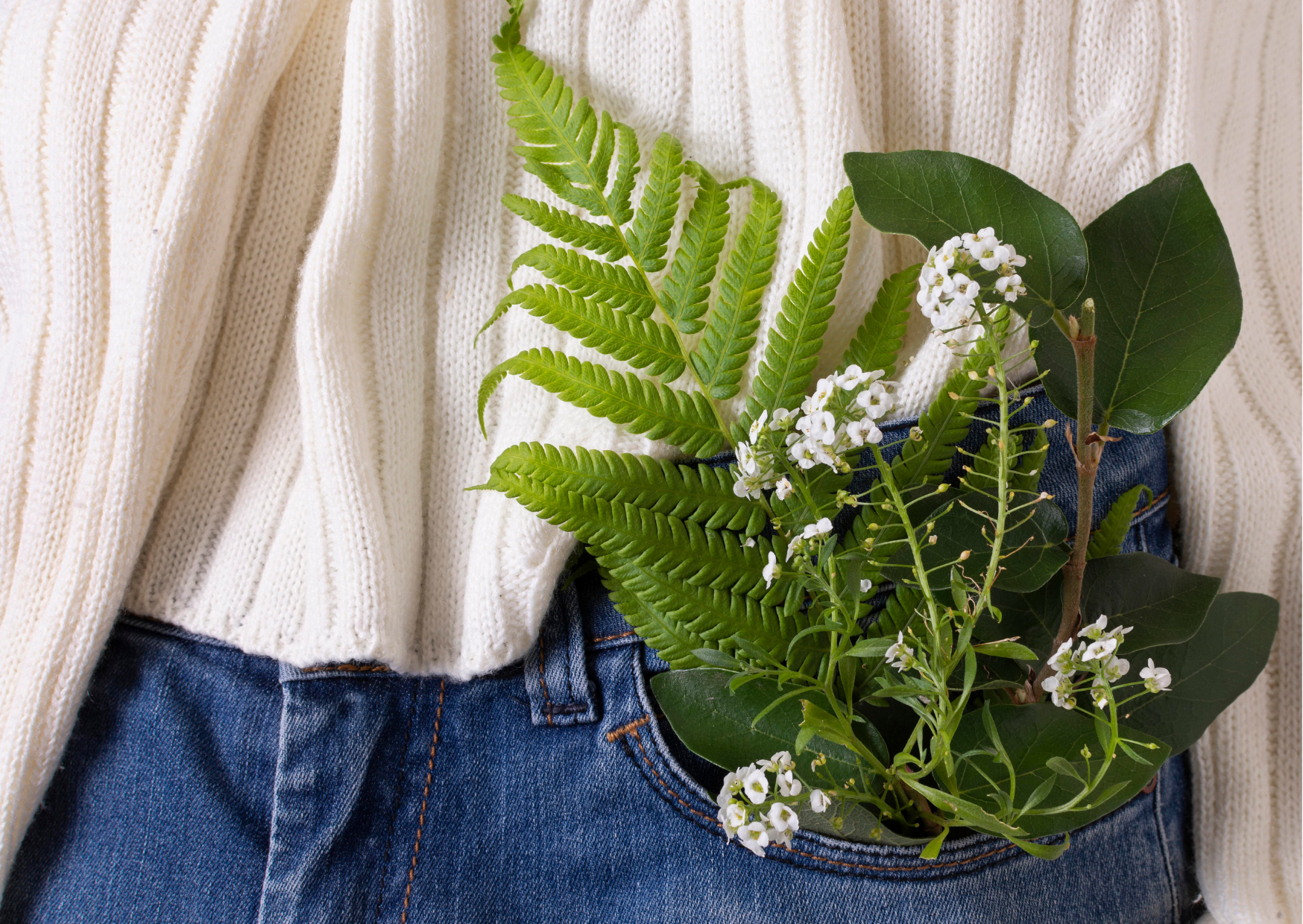 A woman wearing jeans and a jumper with foliage in her pocket