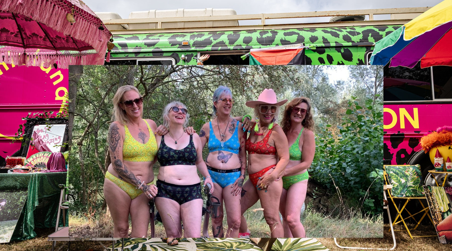 five women wearing brightly coloured patterned matching underwear pose in an outdoor setting. behind is a photo of a brightly coloured leopard print bus with parasols outside.