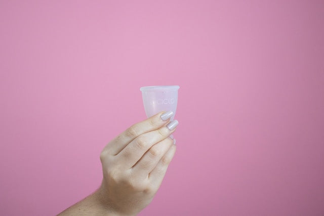 A hand holding up a menstrual cup with a pink background 