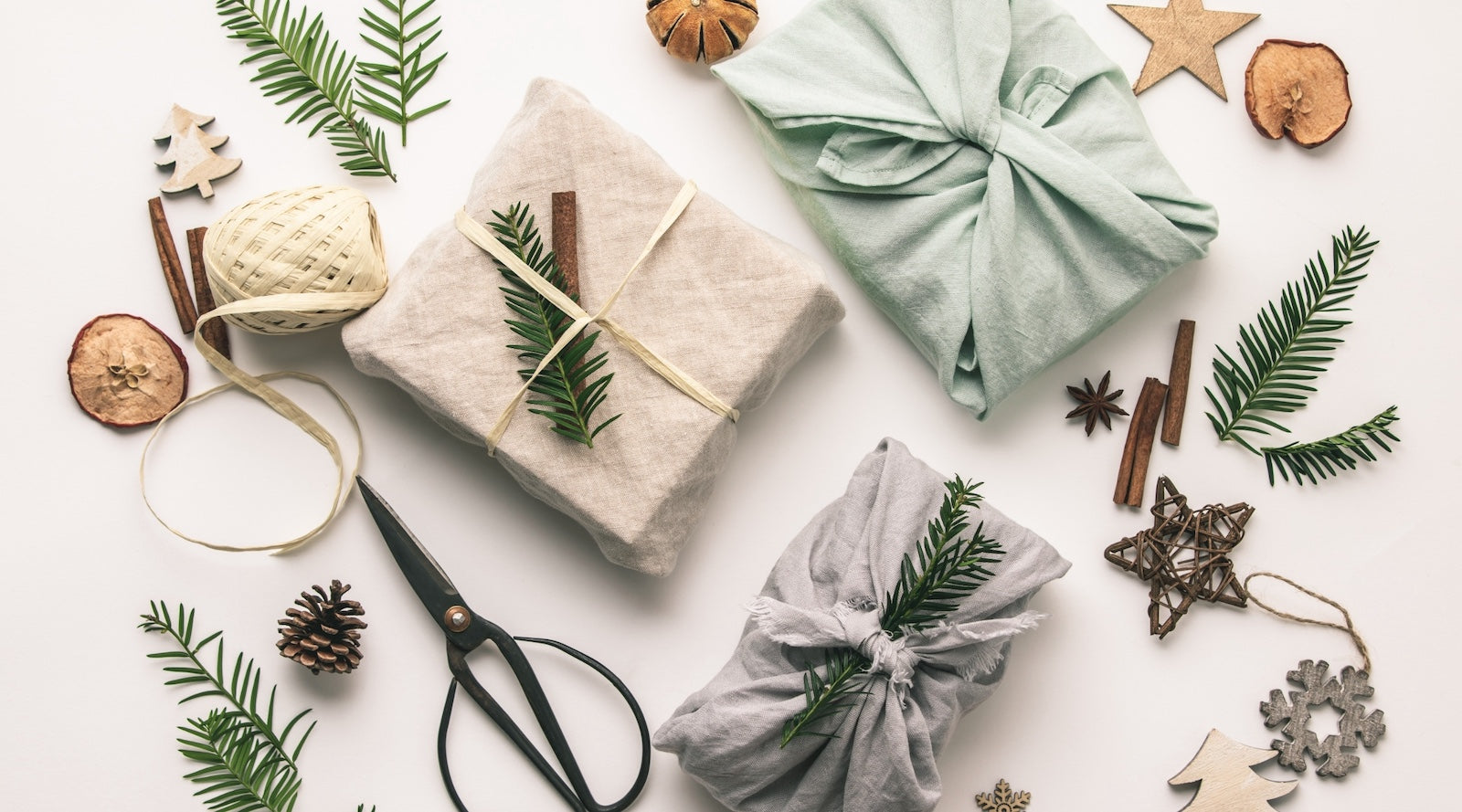 flatlay photo of three presents wrapped in fabric with decorations, scissors, and dried fruit scattered around