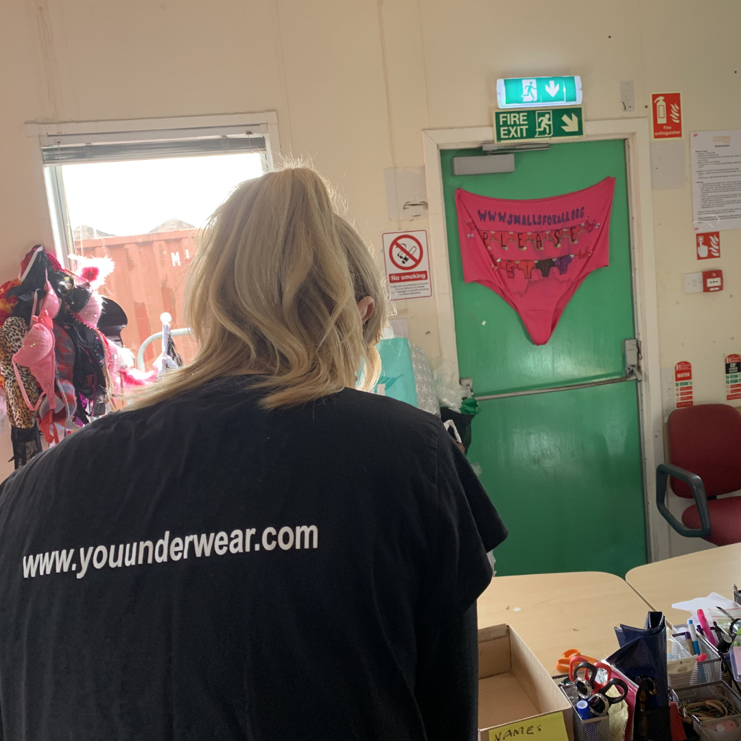 Sarah is turned away from the camera, helping to sort underwear whilst wearing a y.o.u underwear t-shirt
