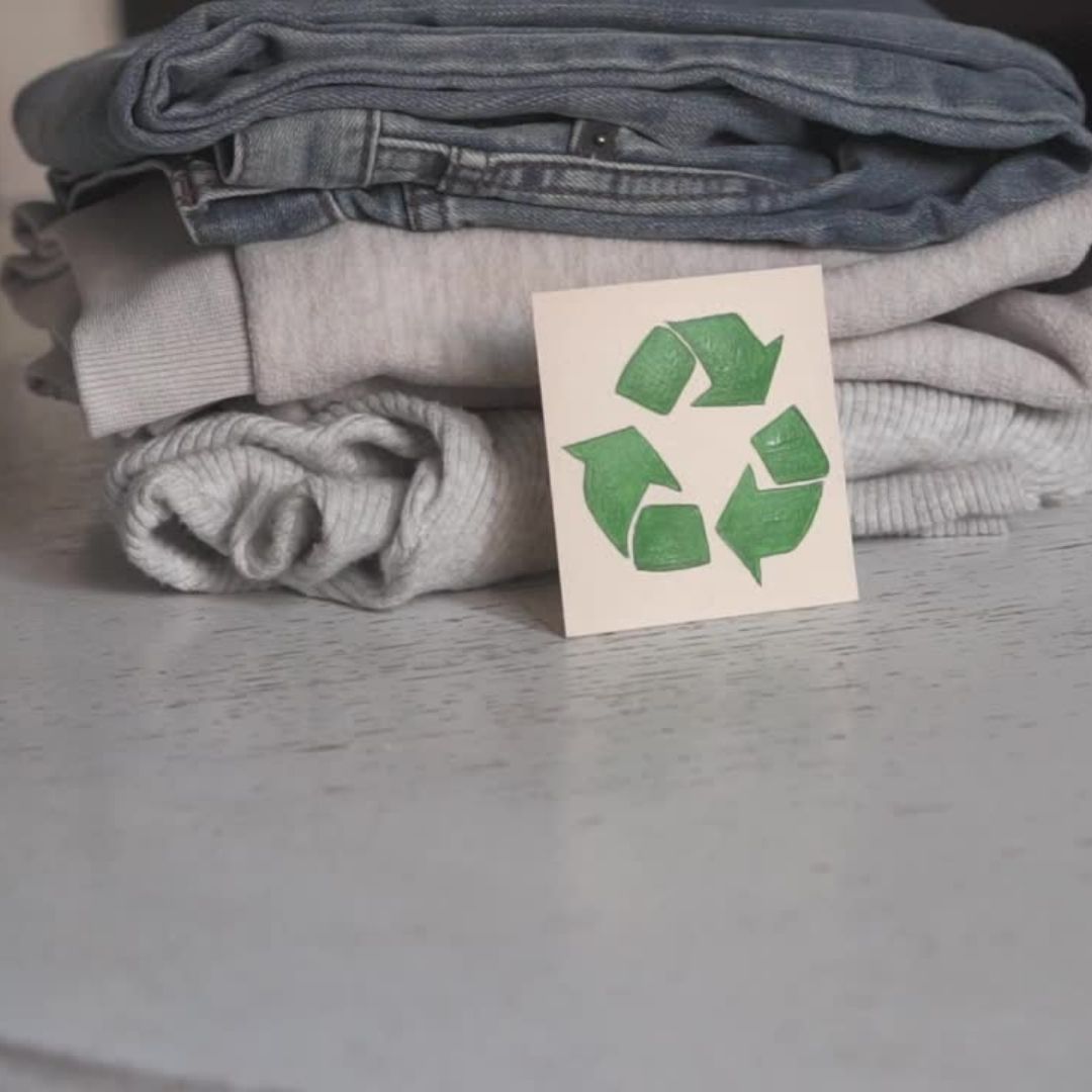 In front of a pile of jeans and white jumpers, a handdrawn green recycling logo is propped up