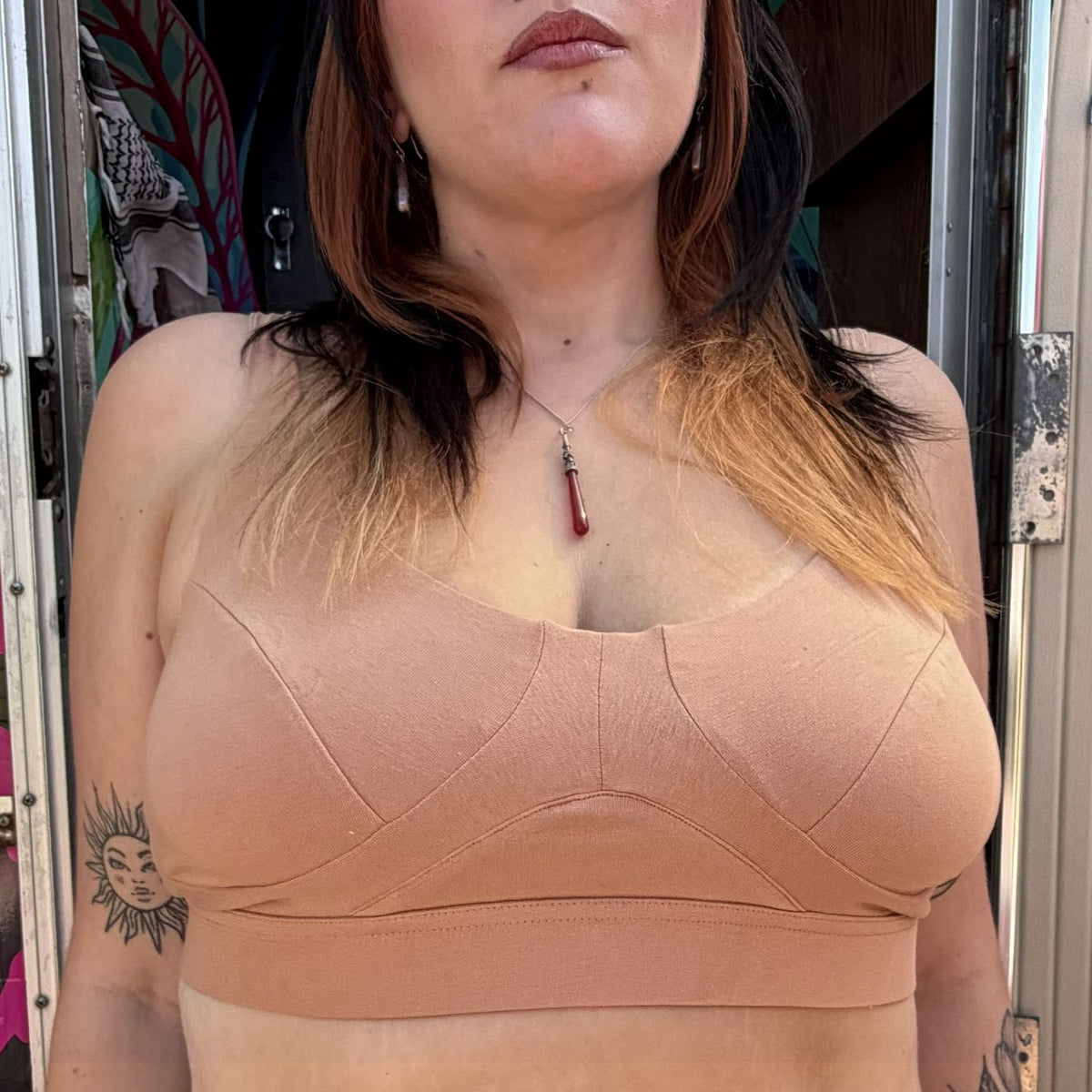 A photo of a model wearing the YOU Underwear non wired bra in almond. She is standing facing the camera and the photo is zoomed so we can see from her lips to just below her bust. 