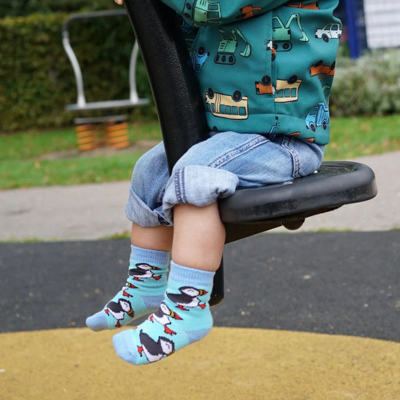 A photo of a child on a swing in a play park wearing the bare kind kids puffin socks