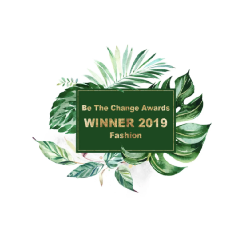 An image which reads 'Be The Change Awards Winner 2019 Fashion,' in gold bold writing. The background is white and there is a green foliage graphic in the center, where the text is positioned in a dark green text box.