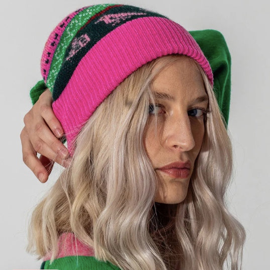 A female model wearing Black & Beech fairisle beanie in bubblegum pink whilst holding her arm over her head in a pose
