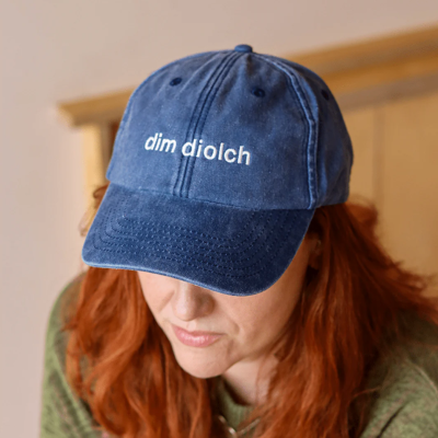 A model wearing the Black & Beech Dim Diolch baseball cap in denim blue 
