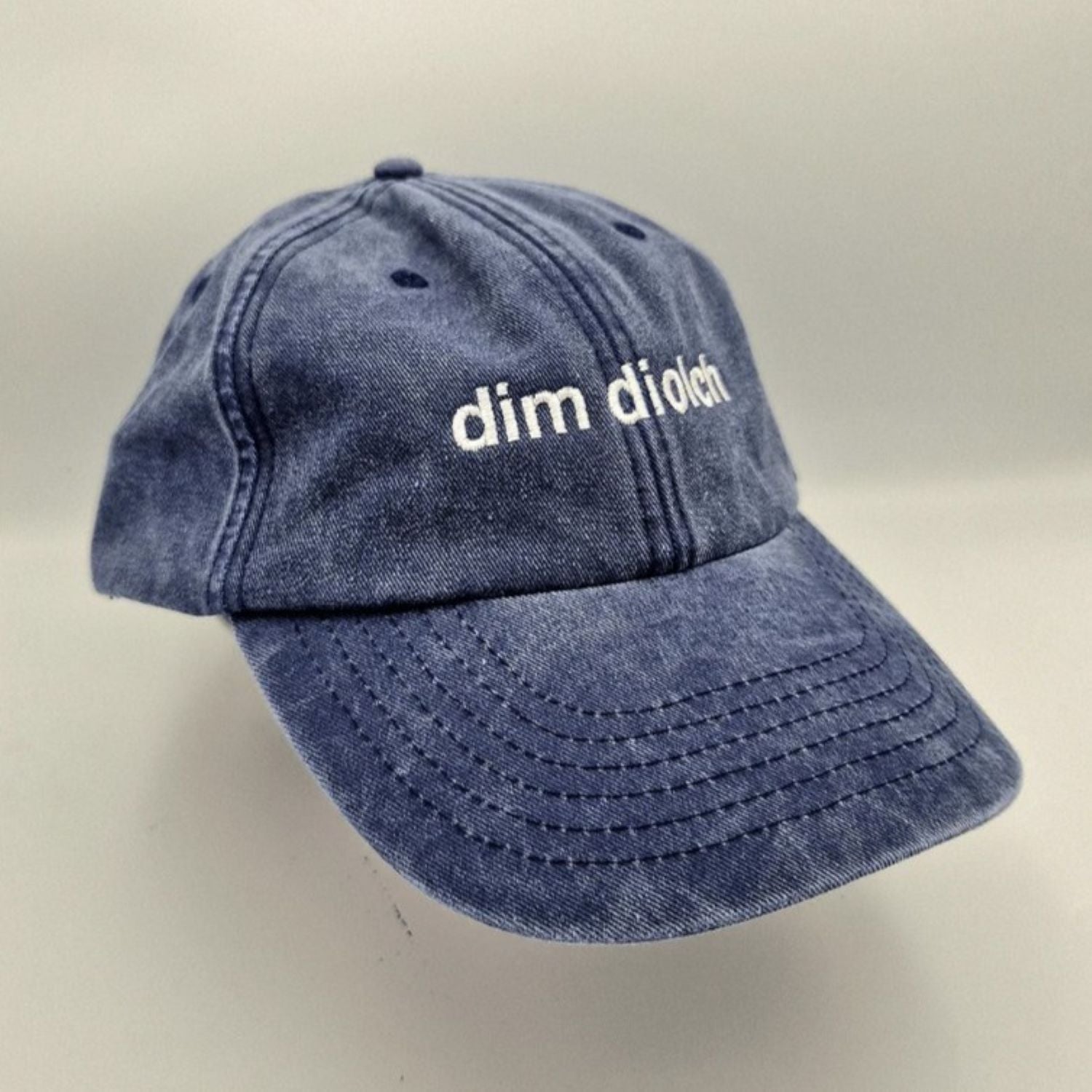 A photo of the Black & Beech Dim Diolch baseball cap in denim blue on a white background