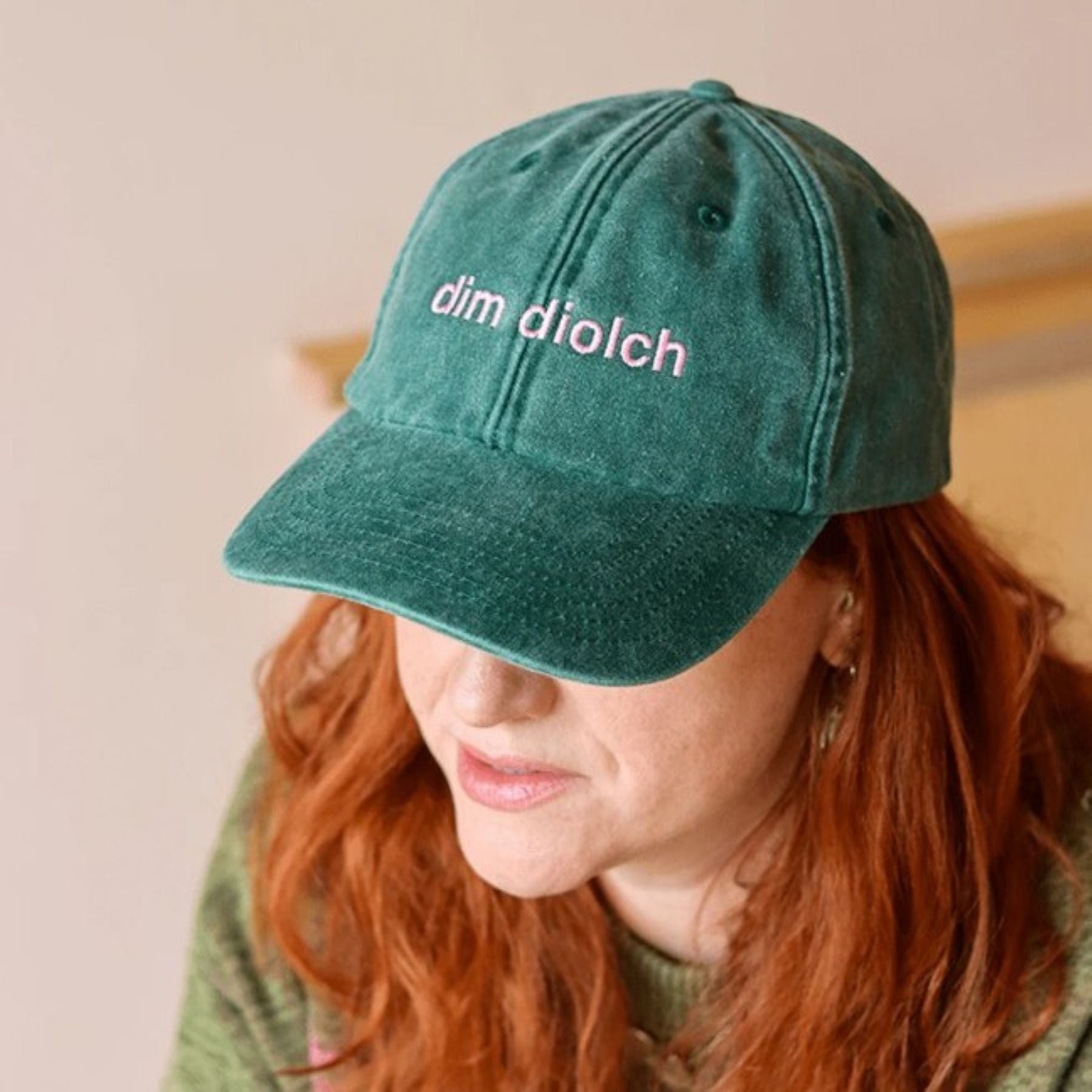 A model wearing the Black & Beech Dim Diolch baseball cap in forest green