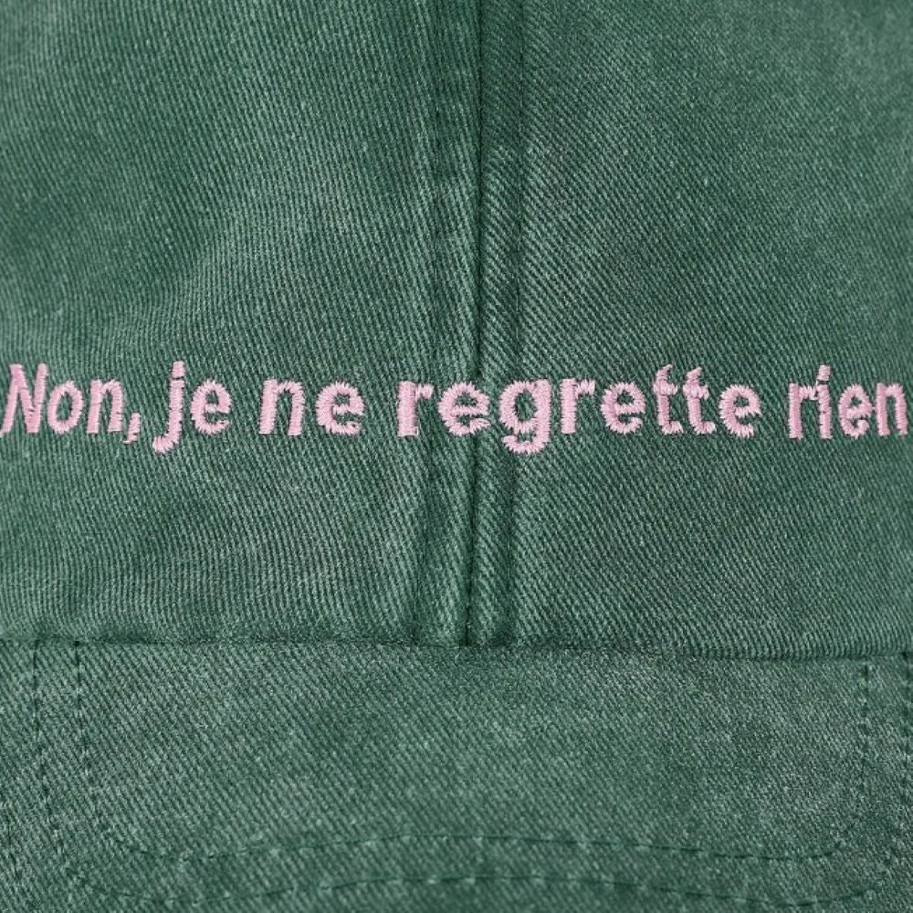 A close up of the Black & Beech Non Regrette cap in forest green with baby pink writing