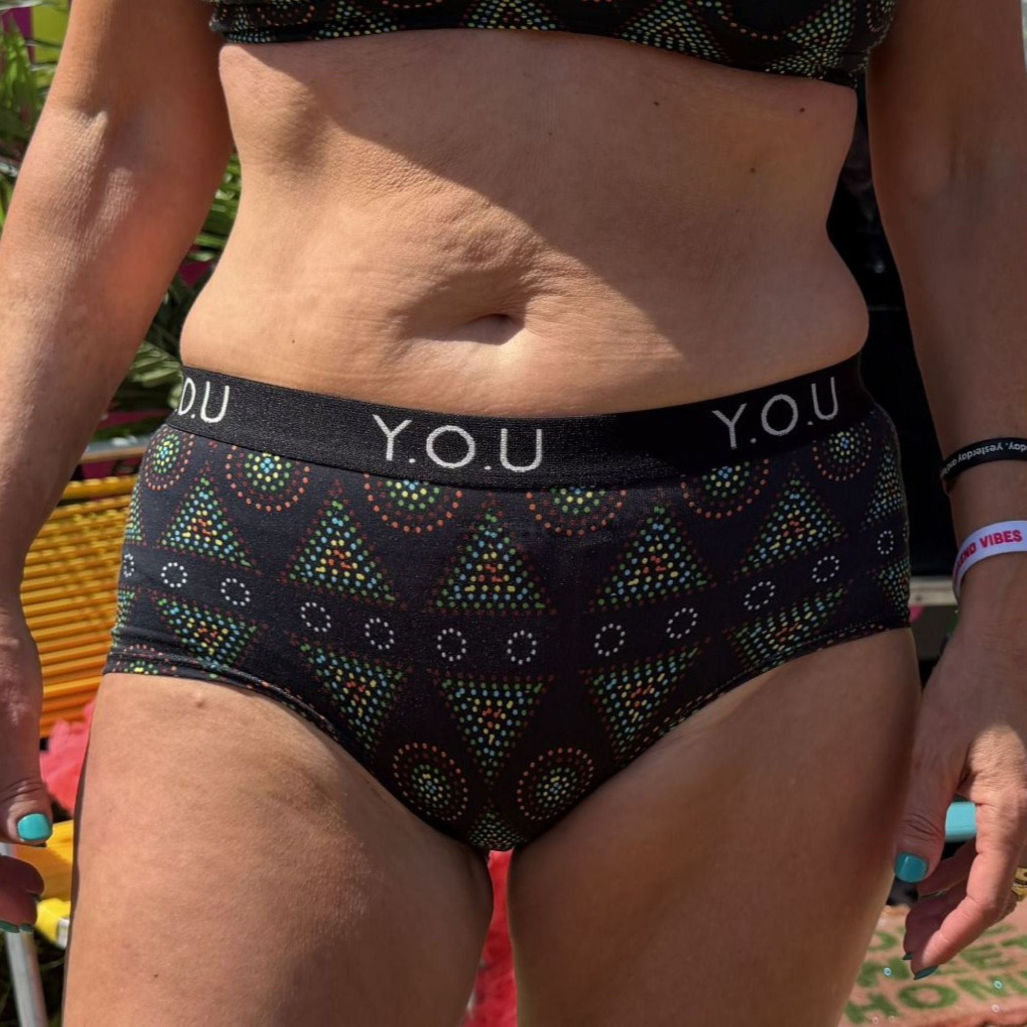 A close up photo of a model wearing the YOU Underwear boyshorts with you elastic in black mara. The photo is zoomed in so we can see from the model's upper stomach to their mid thigh. They are facing the camera with their hands sides.
