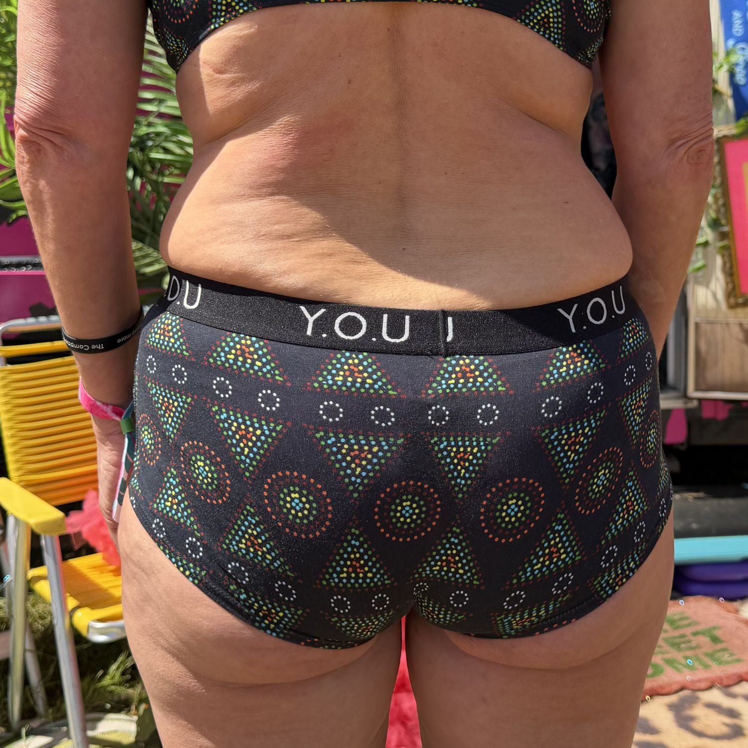 A close up photo of a model wearing the YOU Underwear boyshorts with you elastic in black mara. The photo is zoomed in so we can see from the model's upper stomach to their mid thigh. They are facing away from the camera with their hands sides.