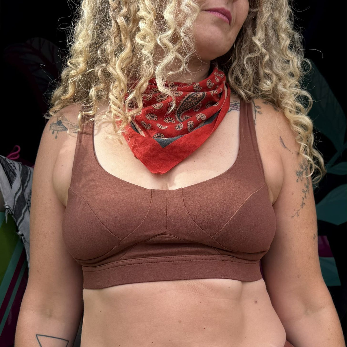 A photo of a model wearing the YOU Underwear non wired bra in chestnut. She is standing facing the camera with her arms at her sides and has long curly blonde hair. She is also wearing a red neck scarf and the photo is zoomed in so we can see from her lips to her mid-stomach.