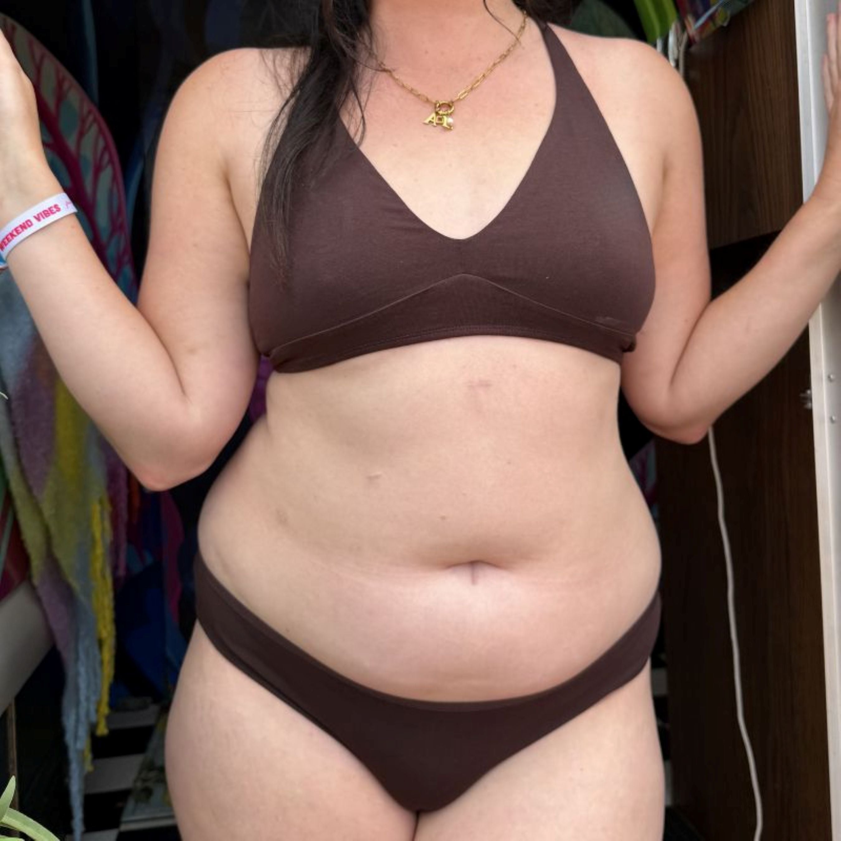 Close up image of model wearing YOU Underwear Bralette and Low Rise Bikini Matching Set in Cocoa. The model stands in a doorway, facing the camera. The image shows from below the chin to the upper thigh