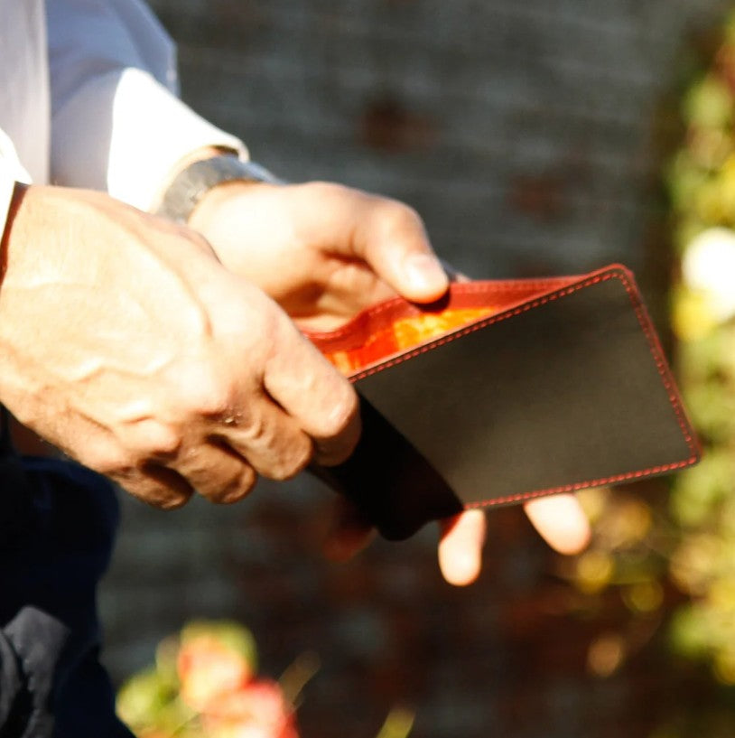 A man holding the Elvis and Kresse black and red Billfold Wallet in front of a brick wall and green bushes