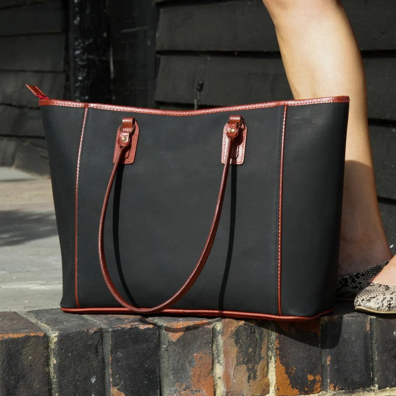 The black and red Elvis and Kresse tote bag placed on the top of a brick wall next to the leg of a model