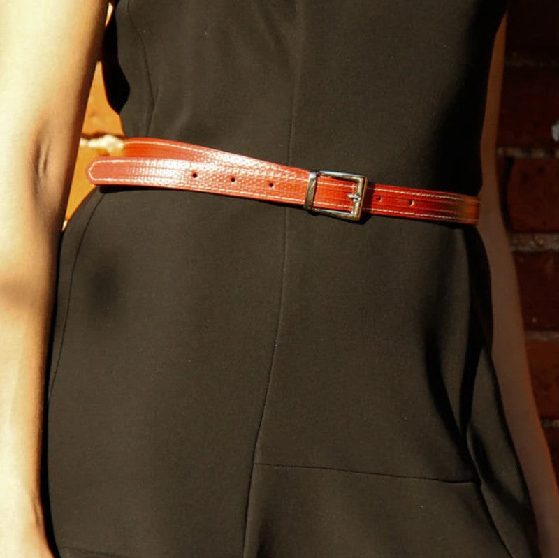 A picture of a model wearing a black dress and the Elvis and Kresse skinny red belt in front of a red brick wall