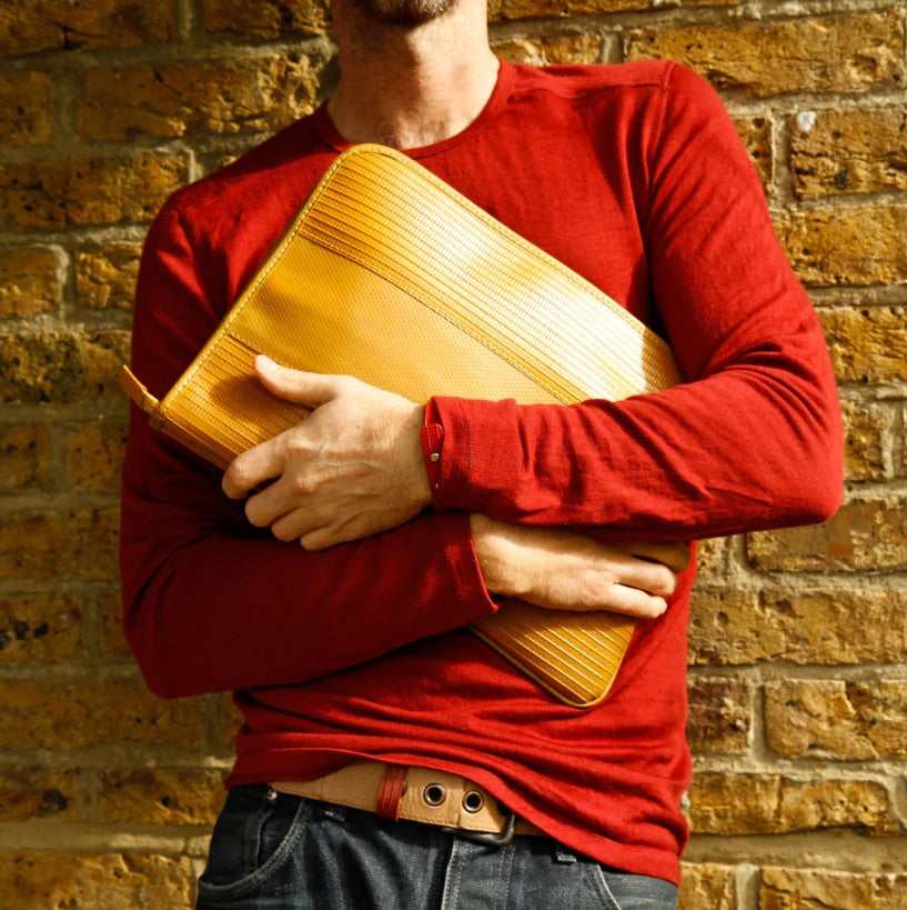 A male model holding the Elvis and Kresse yellow laptop case whilst leaning on a brick wall