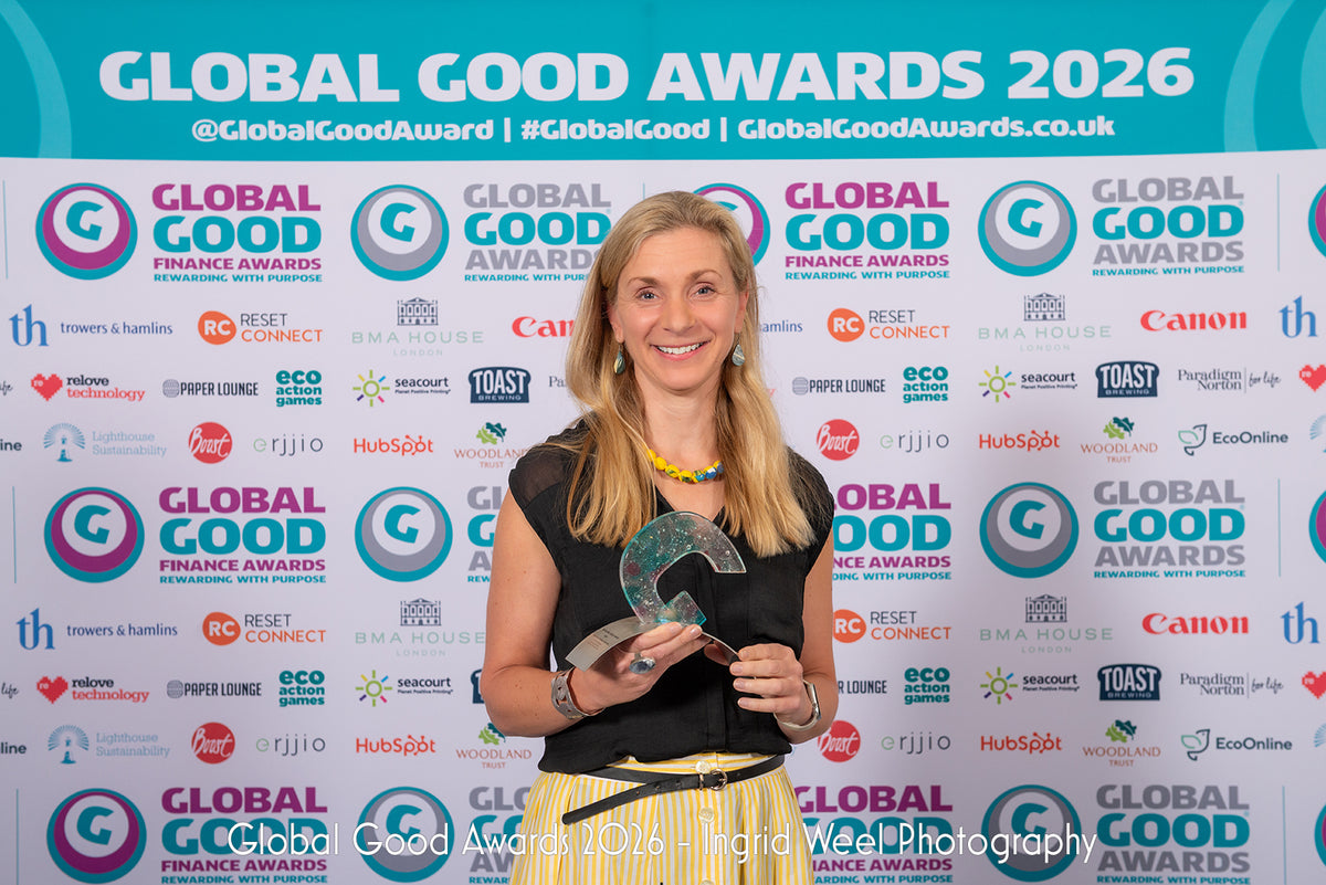 A photo of Sarah Jordan, the founder and CEO of YOU Underwear standing and holding the winning trophy for the Global Good Awards 2026. She is standing facing the camera, smiling and behind her there is a wall branded with the Global Good Awards advertising.