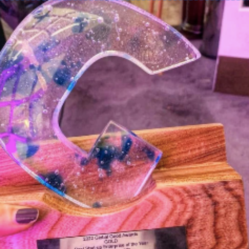 A picture of a Global Good Award Trophy. There is a big Glass letter G on a wooden podium.